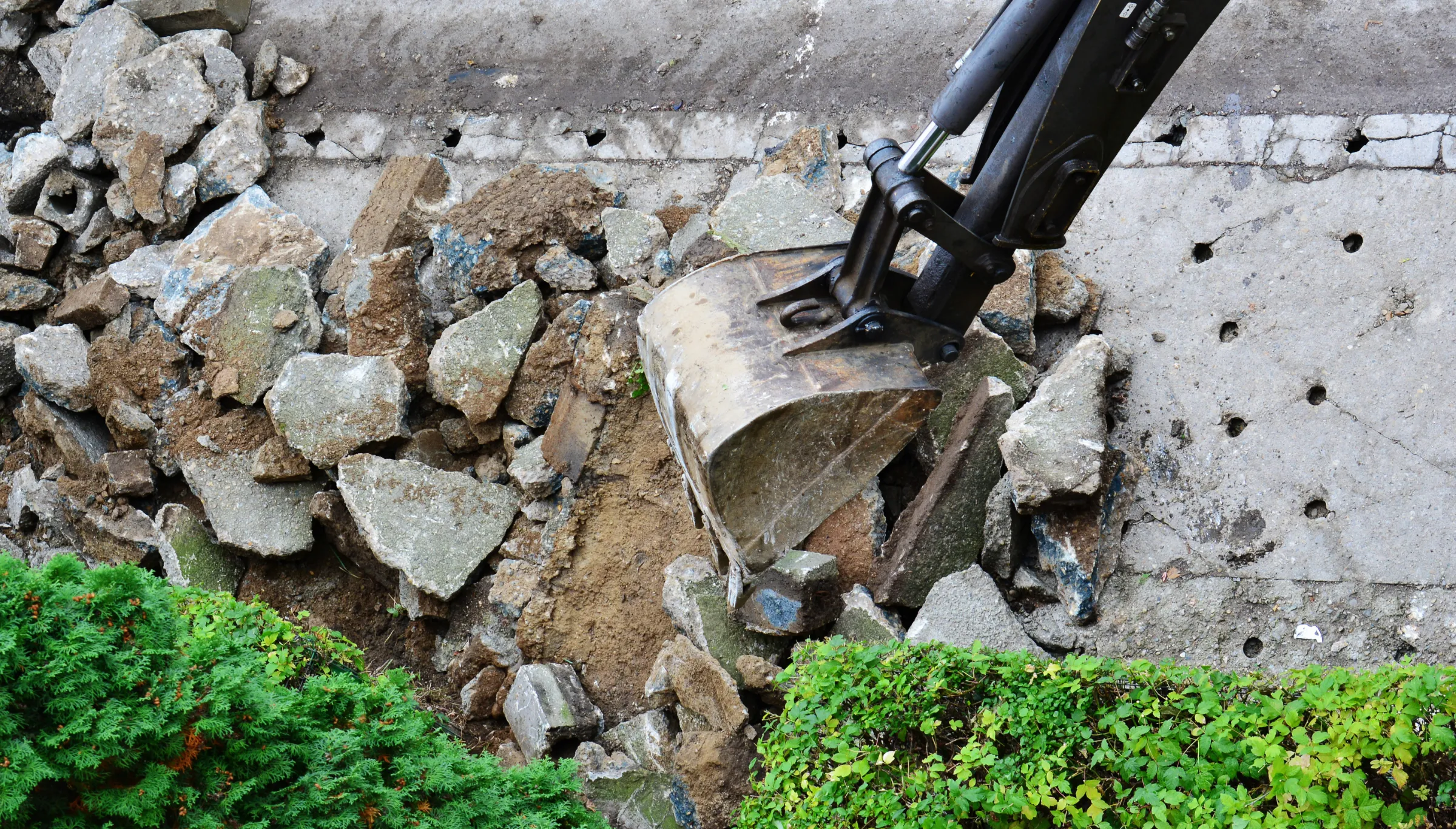 Concrete slab demolition in Dallas TX with excavator breaking foundation and removing concrete during site preparation project