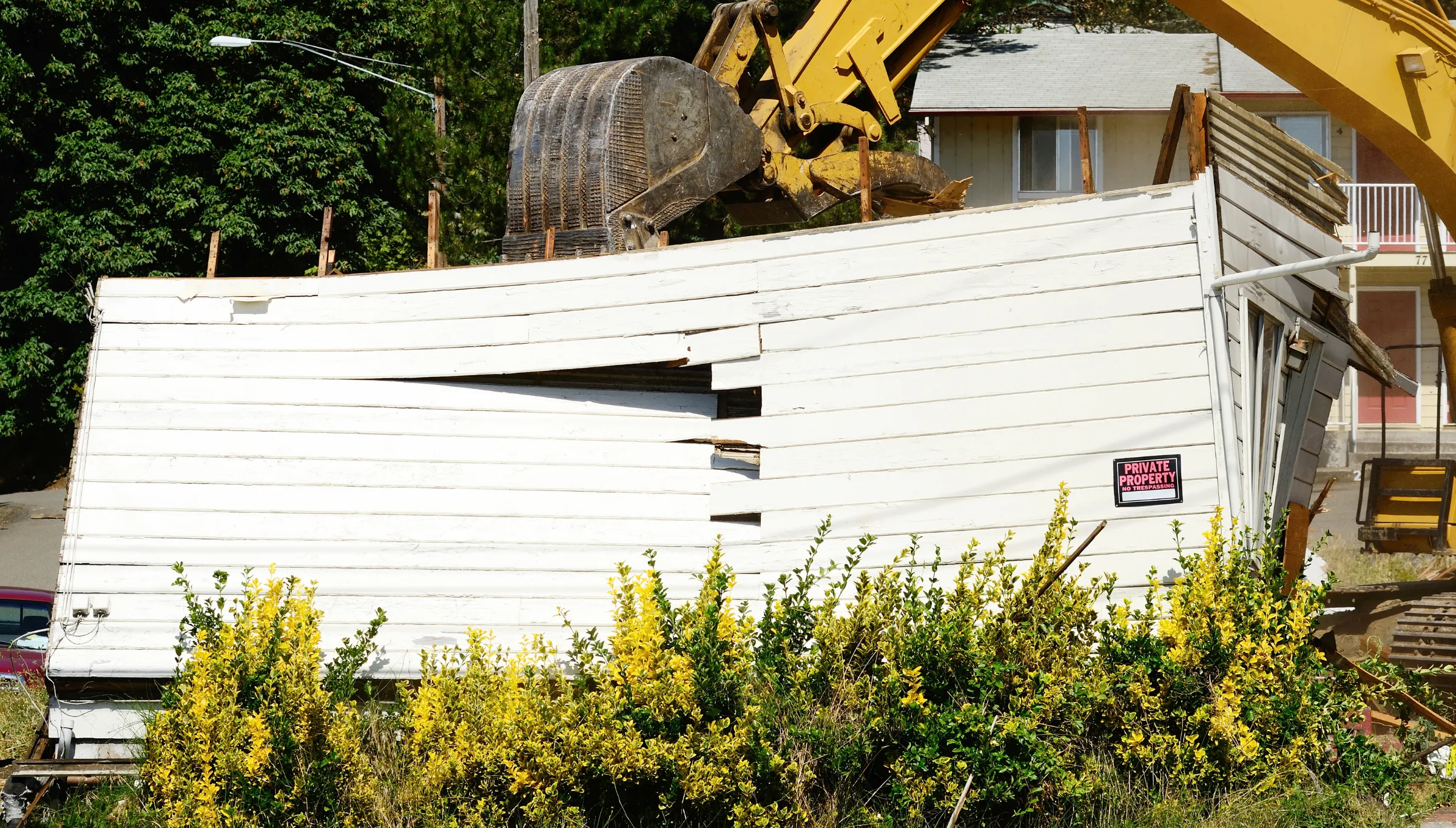 Residential demolition in Dallas TX with excavator tearing down house structure during complete home teardown project